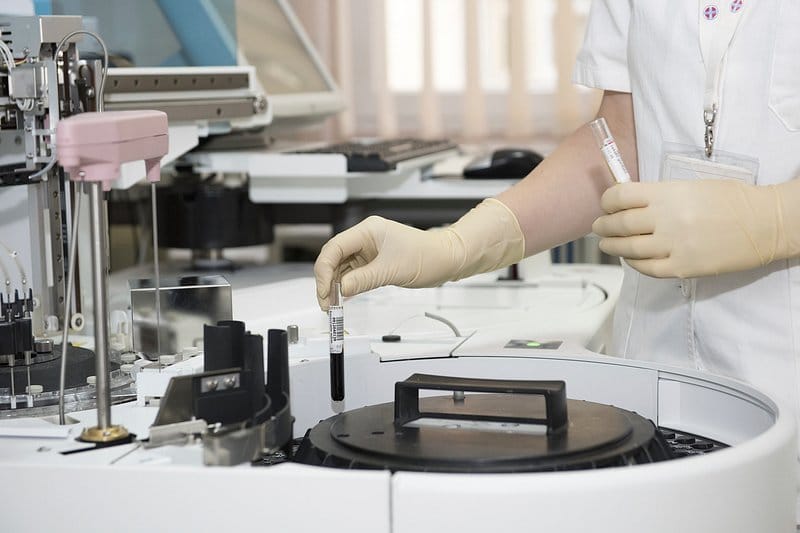 Gloved laboratory professional handling samples at an automated analyzer